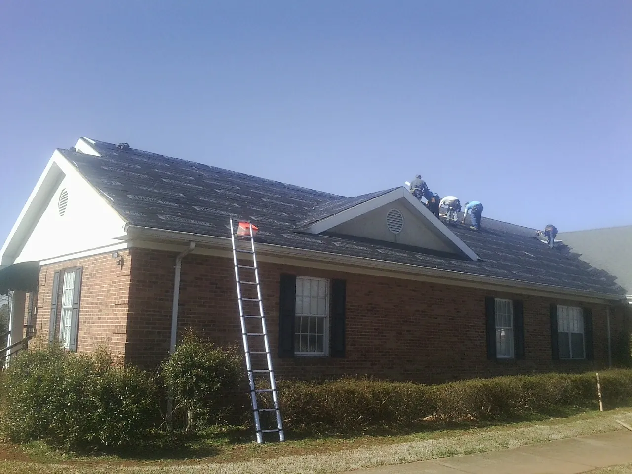 Crew tearing shingles off a brick ranch roof with a ladder set — Emergency Roof Repair work by our crew in Westpoint