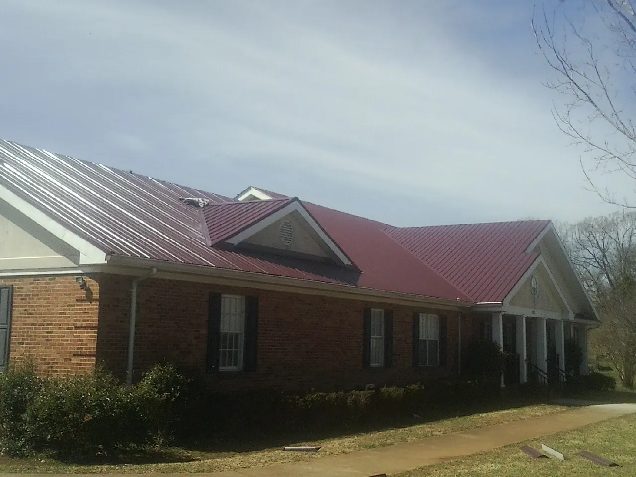 Red metal roof with gabled entries on a long brick building, from a Hail Damage Roof Repair job in Westpoint