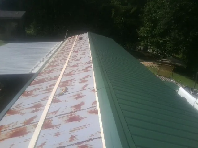Old rusted panels beside newly installed green metal roofing — Wind Damage Roof Repair by Roofing Brothers in Westpoint