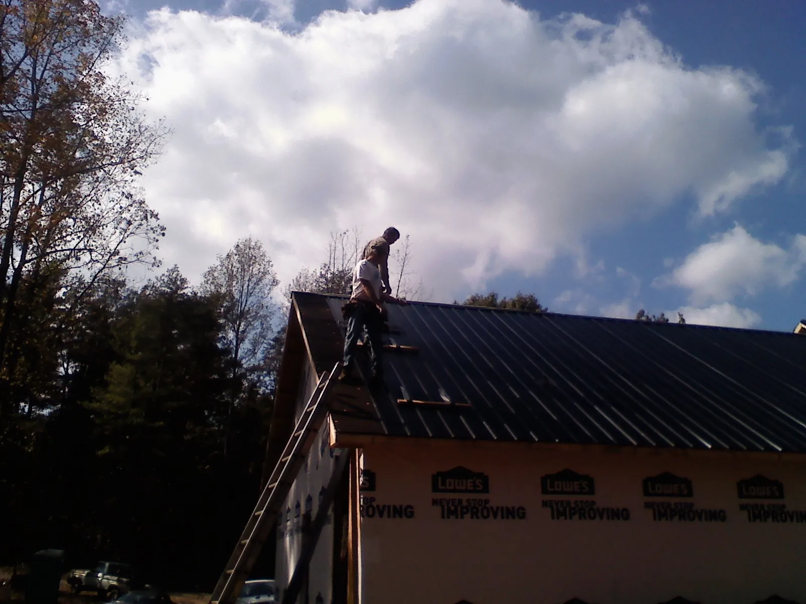 Roofer fastening dark metal panels high against a cloudy sky, from a Roof Inspection job in Westpoint